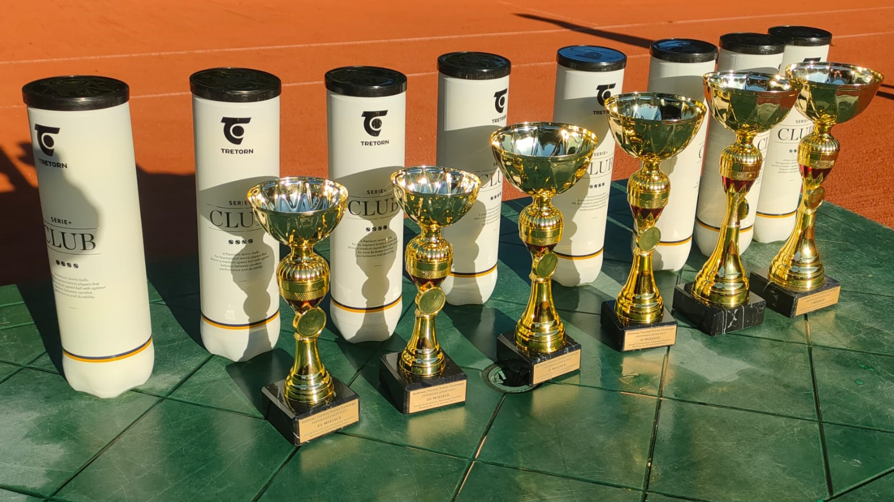 Puchary i nagrody w postaci piłek postawione na zielonym stoliku.